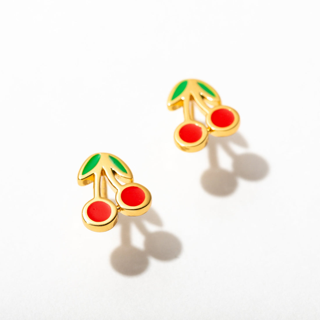 Gold cherry-shaped earrings with red stones on a white background