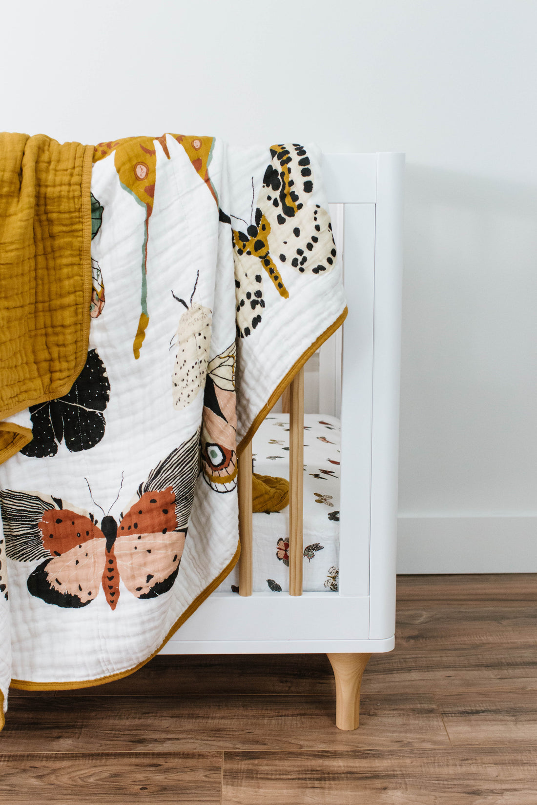 Butterfly-patterned quilt draped over a white cabinet with wooden legs on a wooden floor.
