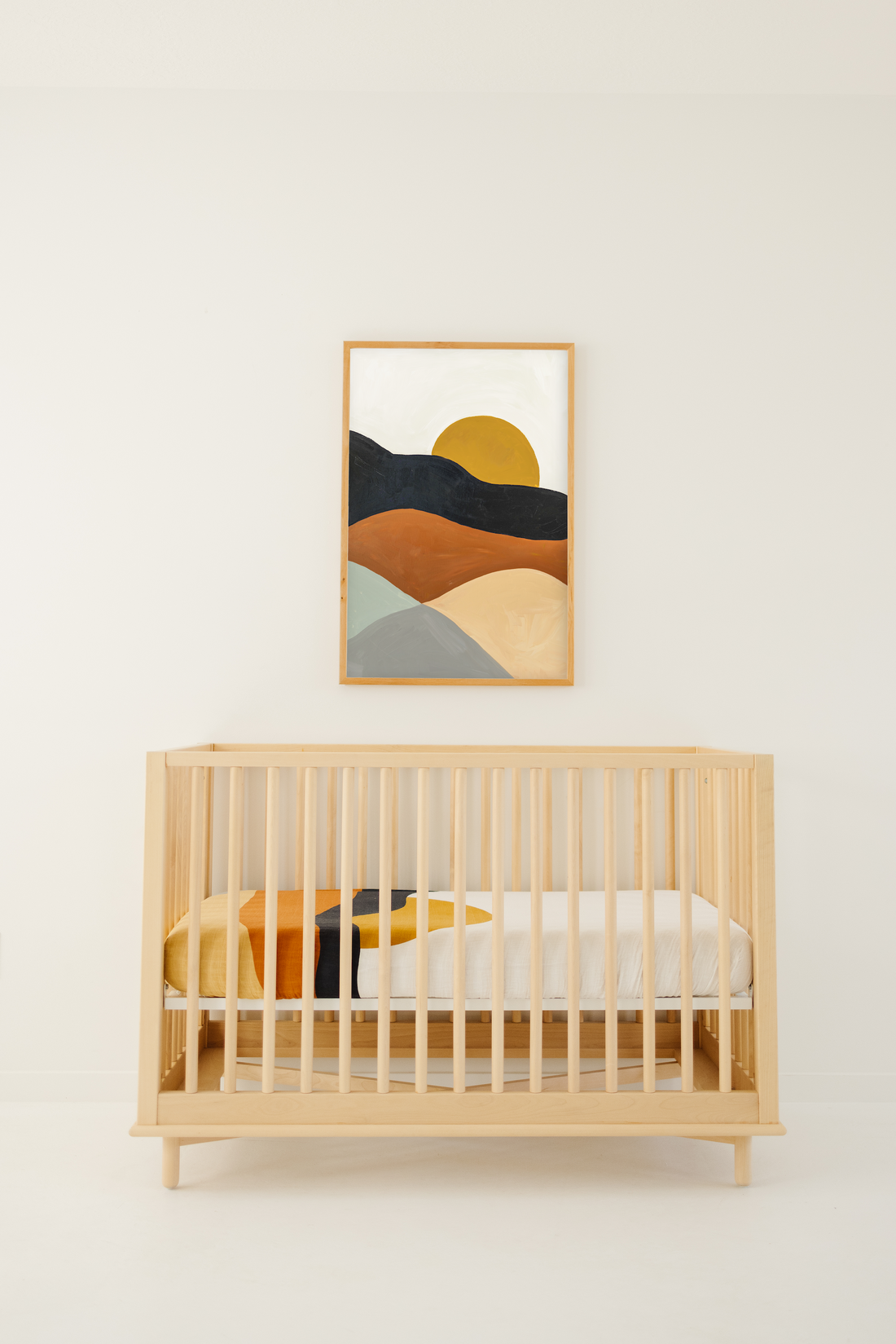 Wooden crib with colorful bedding in a room with a abstract wall art