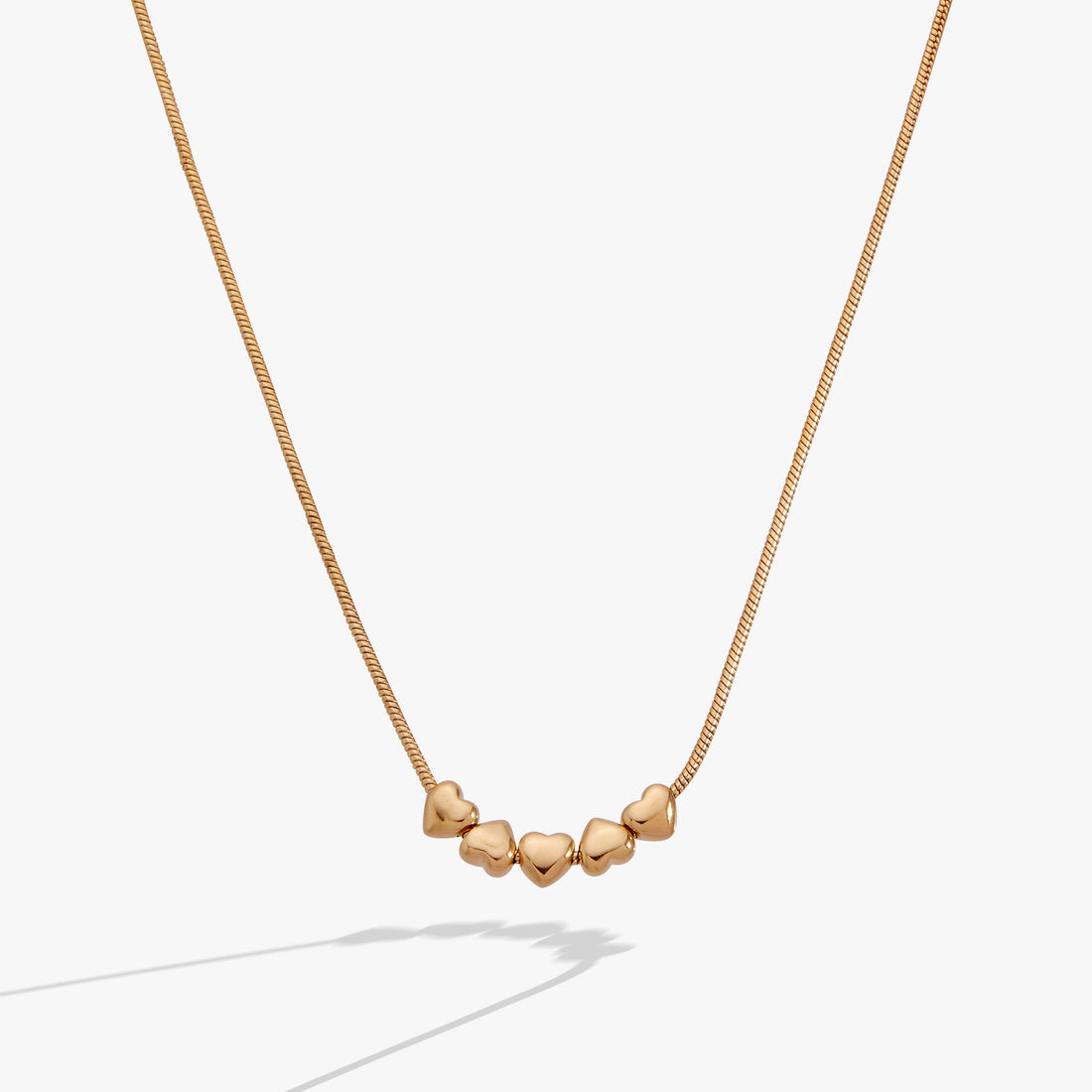 Gold necklace with heart-shaped pendants on a light gray background