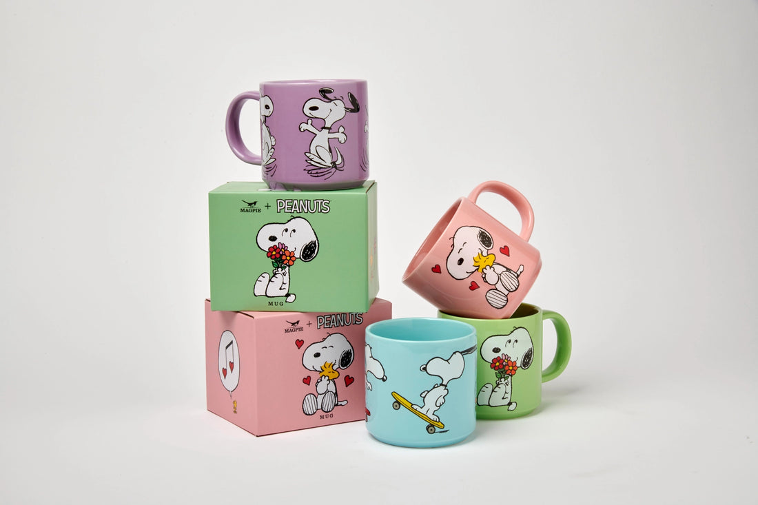 A collection of ceramic mugs with colorful Peanuts character designs, stacked on top of each other.