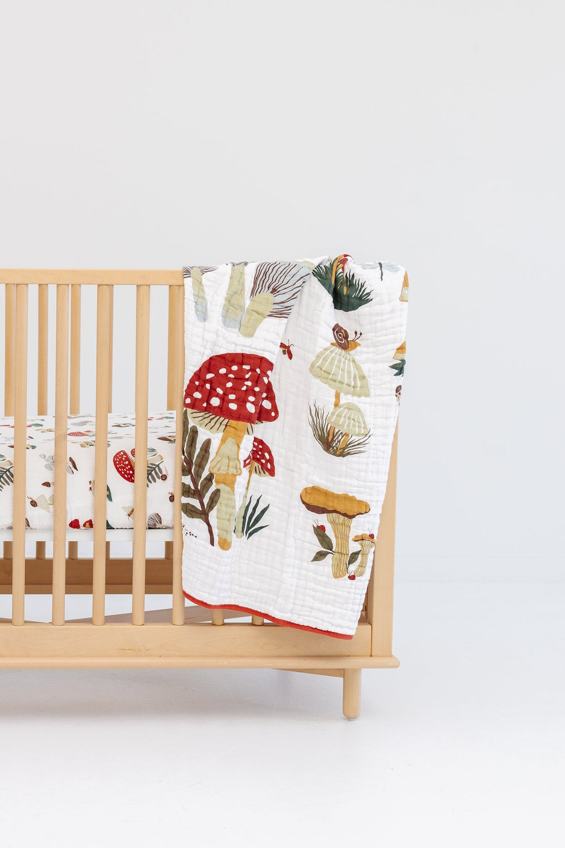 Wooden crib with a colorful mushroom-patterned quilt draped over it on a white background