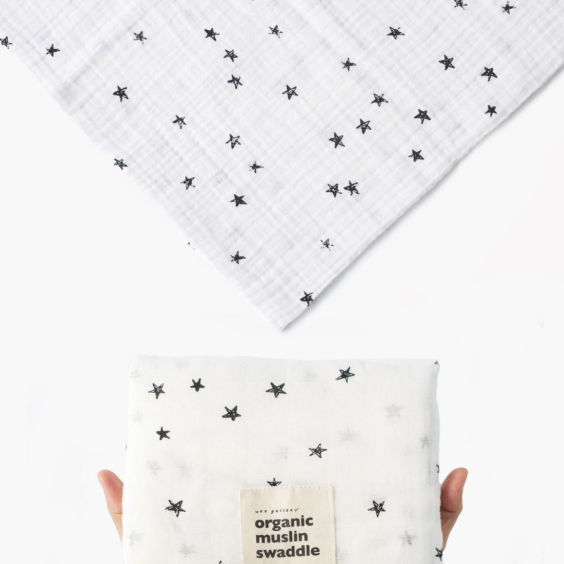 White organic muslin swaddle with black star pattern held by a hand on a white background