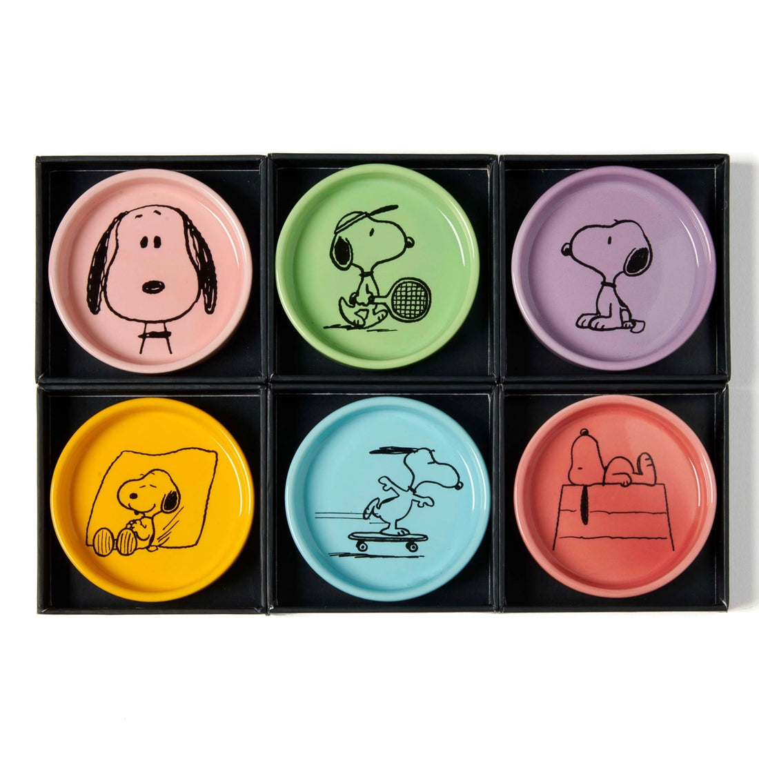 A collection of six colorful ceramic dishes with Peanuts characters, each dish has a different background color and features an illustration of Snoopy in various playful poses. The dishes are displayed in a slide-out box.
